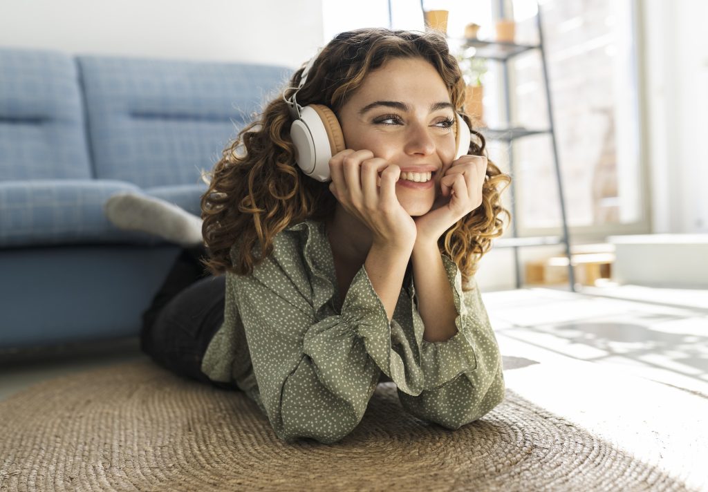 pretty curly-haired woman lying on the floor at home listening to music happy smiling relaxed